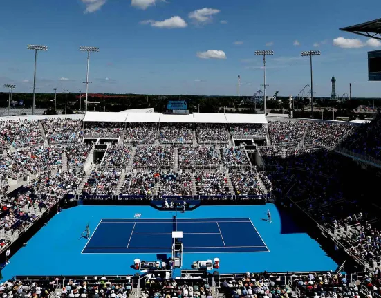 Vista aérea de una pista de tenis dura azul con las gradas llenas.