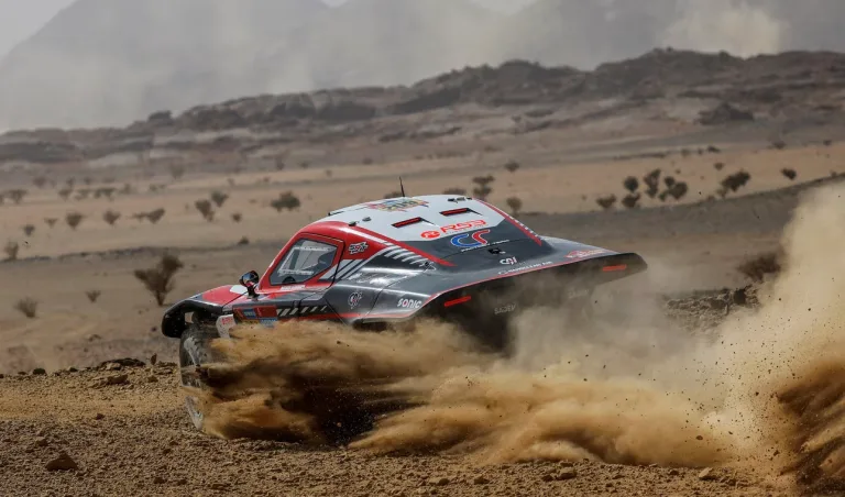 Vehículo de rally levantando polvo sobre un terreno desértico.
